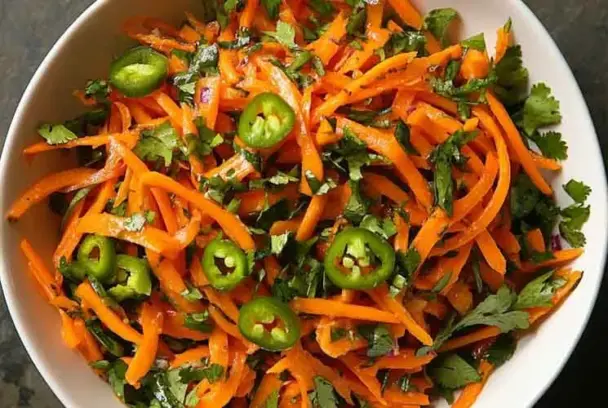Top view of a vibrant shredded carrot and serrano chile salad with chopped cilantro, served in a white bowl — colorful, spicy, and fresh.