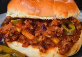 Close-up of a loaded Sloppy Joe sandwich on a soft bun, filled with seasoned ground beef, melted cheddar, diced onions, and sliced jalapeños.