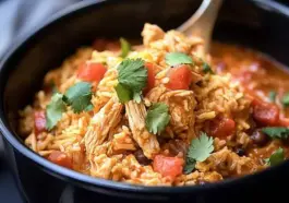 A black bowl filled with slow cooker taco chicken and rice, featuring shredded chicken, diced tomatoes, black beans, and garnished with fresh cilantro.