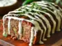 Close-up of sliced jalapeño popper meatloaf on a wooden board, filled with cheese and jalapeños, topped with ranch dressing and chopped fresh herbs.