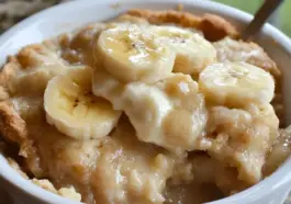 Southern Banana Cobbler in a white dish topped with fresh banana slices and golden crust, showing creamy, gooey filling and baked edges.