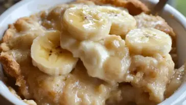 Southern Banana Cobbler in a white dish topped with fresh banana slices and golden crust, showing creamy, gooey filling and baked edges.