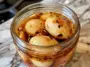 Close-up of spicy pickled eggs in a glass jar filled with chili flake and sesame seed brine, placed on a marbled kitchen counter.