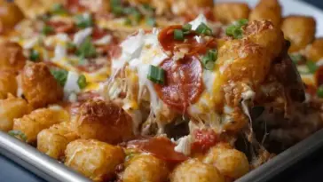 Golden brown tater tots baked over a layer of melted cheese, pizza sauce, and pepperoni, topped with chopped green onions and served hot from a casserole dish.