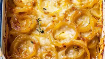 Close-up of golden-baked Tennessee Onions with melted cheese and sweet caramelized onion rings in a white baking dish, garnished with fresh thyme.