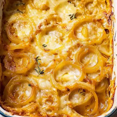 Golden baked Tennessee Onions in a white and blue casserole dish, layered with melted cheese and caramelized sweet onion rings, garnished with fresh thyme.
