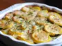 Creamy baked zucchini and yellow squash au gratin in a white dish, topped with melted cheese, herbs, and golden brown edges.