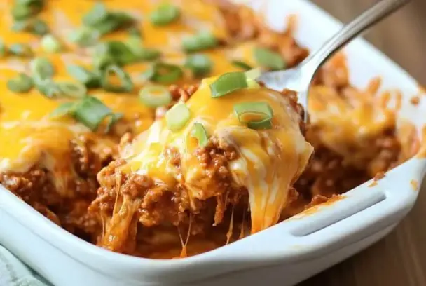 Freshly baked Sloppy Joe Casserole with melted cheese and green onions being scooped from a white casserole dish, showing its cheesy, savory layers.