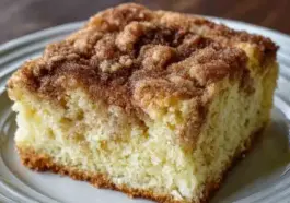 Close-up of a thick slice of Amish Cinnamon Sugar Coffee Cake with a cinnamon sugar crust and soft, fluffy interior on a white plate.