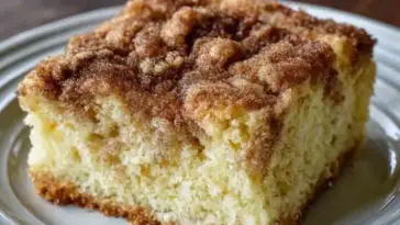 Close-up of a thick slice of Amish Cinnamon Sugar Coffee Cake with a cinnamon sugar crust and soft, fluffy interior on a white plate.