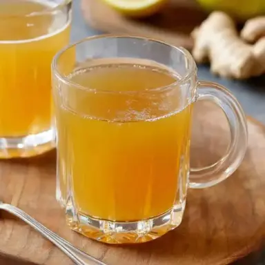 A glass mug filled with apple cider vinegar weight loss drink on a wooden board, surrounded by lemon, apple, and fresh ginger.