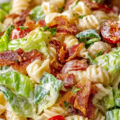 Close-up of creamy BLT pasta salad with rotini pasta, crispy bacon, romaine lettuce, cherry tomatoes, and ranch dressing in a white bowl