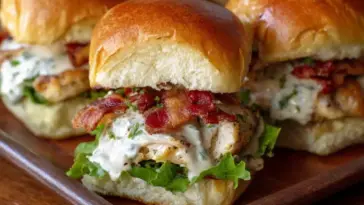 Close-up of bacon ranch chicken sliders layered with crispy bacon, ranch dressing, lettuce, and grilled chicken on golden, soft slider buns.