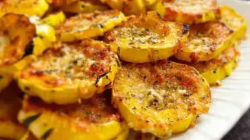 Plate of golden-brown baked Parmesan squash slices with a crispy cheese coating, arranged neatly on a white serving dish.