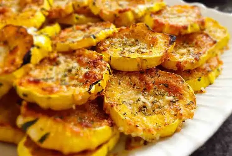Plate of golden-brown baked Parmesan squash slices with a crispy cheese coating, arranged neatly on a white serving dish.