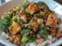 Close-up of beef and broccoli stir fry served on a bed of white rice, featuring glazed beef pieces, vibrant broccoli, chopped green onions, and sesame seeds in a savory brown sauce.