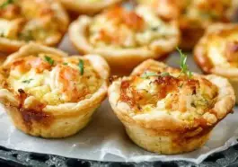 Tray of freshly baked cheddar crab and shrimp mini quiches with flaky crusts, topped with herbs and melted cheese, ideal for party appetizers or brunch.