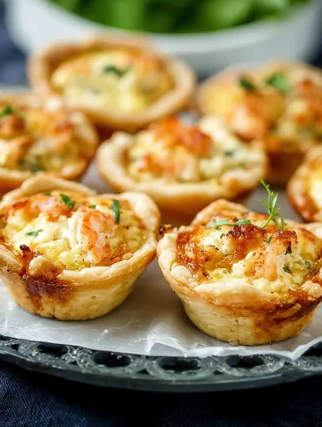 Close-up of golden-baked cheddar crab and shrimp mini quiches in flaky crusts, garnished with herbs, served on a tray for brunch or appetizers.