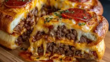 Sliced cheesy pizza burger pie on a wooden board, revealing layers of ground beef, melted cheese, pizza sauce, and golden crust topped with pepperoni slices and herbs.