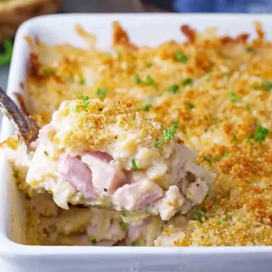 Spoonful of Chicken Cordon Bleu Casserole with creamy sauce, diced ham, and crispy golden breadcrumb topping in a white baking dish.