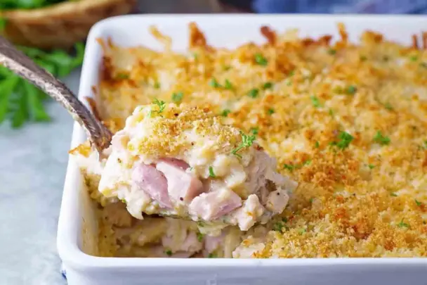 Spoonful of Chicken Cordon Bleu Casserole with creamy sauce, diced ham, and crispy golden breadcrumb topping in a white baking dish.