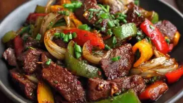 Plate of Chinese Pepper Steak featuring sliced beef, green and red bell peppers, sautéed onions, and thick savory sauce, garnished with chopped scallions.