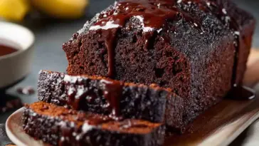 Sliced loaf of moist chocolate banana bread drizzled with melted chocolate on a wooden serving board, showcasing its rich, fudgy interior and glossy topping.