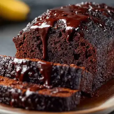 Sliced loaf of moist chocolate banana bread drizzled with melted chocolate on a wooden serving board, showcasing its rich, fudgy interior and glossy topping.