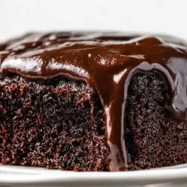 Close-up of a rich and moist Chocolate Depression Cake with glossy chocolate frosting dripping over the edges, served on a white plate.