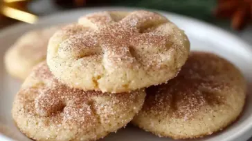 Close-up of soft cinnamon sugar cookies stacked on a white plate, coated in a golden cinnamon-sugar topping with a crackled surface.