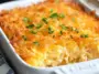 Golden-baked Cracker Barrel Hash Browns Casserole in a white baking dish, topped with melted cheddar cheese and fresh chopped parsley, showing its creamy interior and crispy edges.