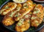 Golden brown crispy ranch chicken fillets drizzled with creamy ranch sauce and garnished with fresh parsley, served on a black plate with dipping sauces in the background.