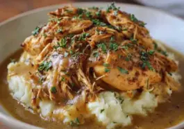 Plate of shredded crockpot chicken in rich brown gravy served over mashed potatoes and garnished with chopped fresh parsley.