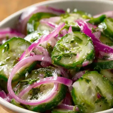 Close-up of a cucumber salad with thinly sliced cucumbers, red onions, and chopped fresh dill in a white bowl, lightly dressed with vinaigrette.