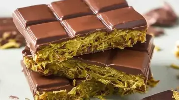 Close-up of stacked homemade Dubai chocolate bars filled with creamy pistachio and crispy golden kataifi pastry, coated in glossy dark chocolate.