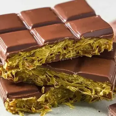 Close-up of stacked homemade Dubai chocolate bars filled with creamy pistachio and crispy golden kataifi pastry, coated in glossy dark chocolate.