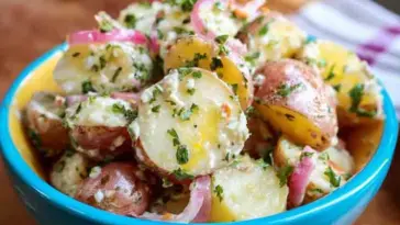 A colorful bowl filled with French Potato Salad made with red and yellow potatoes, sliced red onions, and chopped herbs in a tangy vinaigrette, served in a blue and yellow dish.