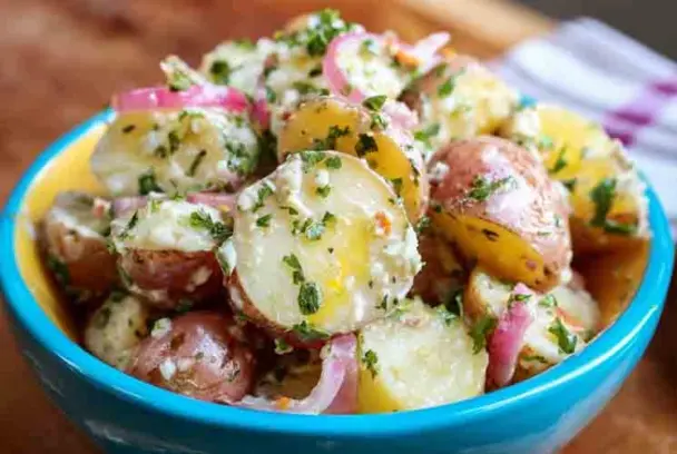 A colorful bowl filled with French Potato Salad made with red and yellow potatoes, sliced red onions, and chopped herbs in a tangy vinaigrette, served in a blue and yellow dish.
