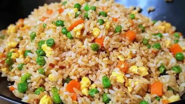 Close-up of homemade fried rice in a black skillet, featuring fluffy rice, shredded carrots, green peas, and scrambled eggs tossed in soy sauce.
