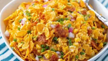 Vibrant bowl of Frito Corn Salad with golden corn chips, red onion, corn, and green onions in a creamy dressing, served with a silver spoon.
