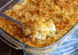 Golden and crispy funeral potatoes in a glass casserole dish, topped with toasted cornflakes and scooped to reveal a creamy, cheesy potato filling.