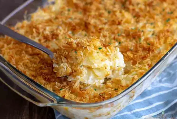 Golden and crispy funeral potatoes in a glass casserole dish, topped with toasted cornflakes and scooped to reveal a creamy, cheesy potato filling.