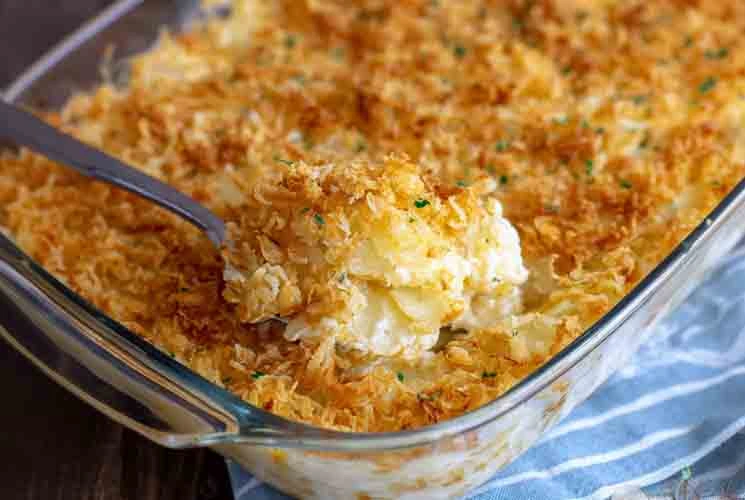 Golden and crispy funeral potatoes in a glass casserole dish, topped with toasted cornflakes and scooped to reveal a creamy, cheesy potato filling.
