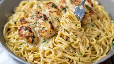 A close-up of creamy Garlic Parmesan Chicken Pasta in a bowl, with golden seared chicken slices on top of linguine tossed in a rich garlic parmesan sauce, garnished with chopped parsley and a fork twirling the noodles.