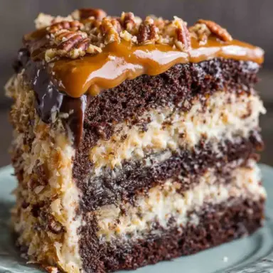 A close-up slice of German chocolate cake layered with rich coconut pecan frosting and topped with glossy caramel and chopped pecans on a ceramic plate.