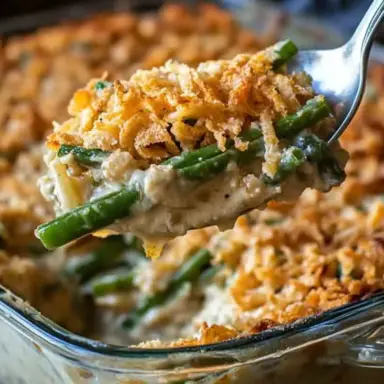 Close-up of a serving of creamy green bean casserole being lifted from a glass baking dish, topped with golden crispy fried onions.