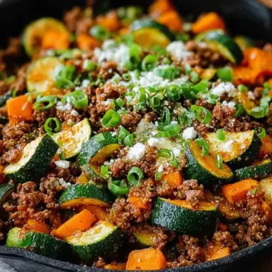 Close-up of a one-pan Ground Beef Zucchini Sweet Potato Skillet topped with green onions and cheese, served in a black cast iron skillet.