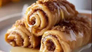 Three honey-drizzled cinnamon roll-ups stacked on a plate, with golden swirls of cinnamon sugar and melted brown sugar topping glistening under warm light.