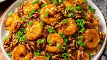 Close-up of crispy Honey Walnut Shrimp topped with chopped green onions and candied walnuts, served over rice on a white plate.
