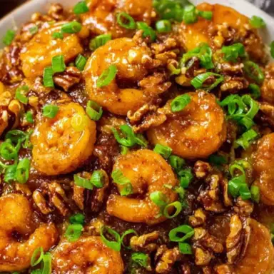 Close-up of crispy Honey Walnut Shrimp topped with chopped green onions and candied walnuts, served over rice on a white plate.